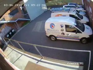 High-quality CCTV security camera footage of a parking lot showcasing branded service vehicles, highlighting the importance of surveillance for commercial building security and property management.