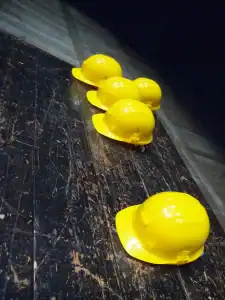 Yellow construction hard hats for safety, displayed on dark textured floor, used in CCTV installation and communication projects, emphasizing safety gear for security and communication workers in industrial settings, image from Tecsec.